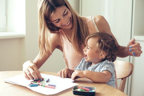 Smiling woman and toddler boy sitting at a table coloring.