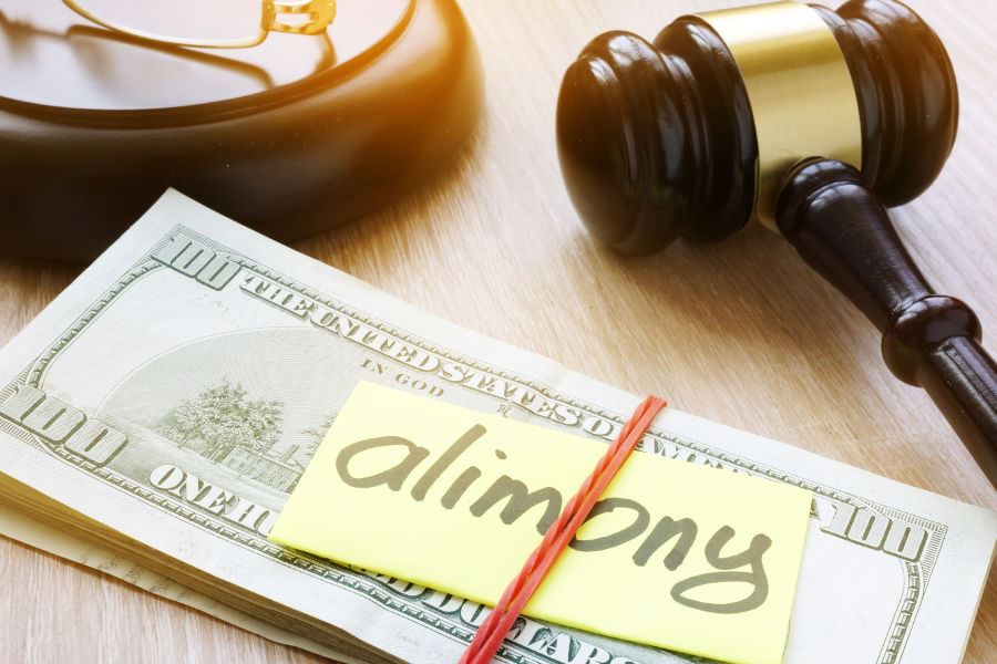 Stack of hundred dollar bills and a note with the word "alimony" on it wrapped with a rubber band.
